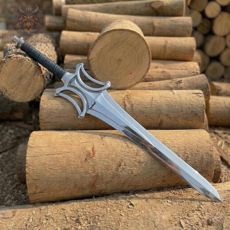 May include: A silver sword with a black handle, resting on a pile of wooden logs. The sword has a distinctive hilt design and a long, sharp blade. The logs are cut and stacked, creating a rustic backdrop.