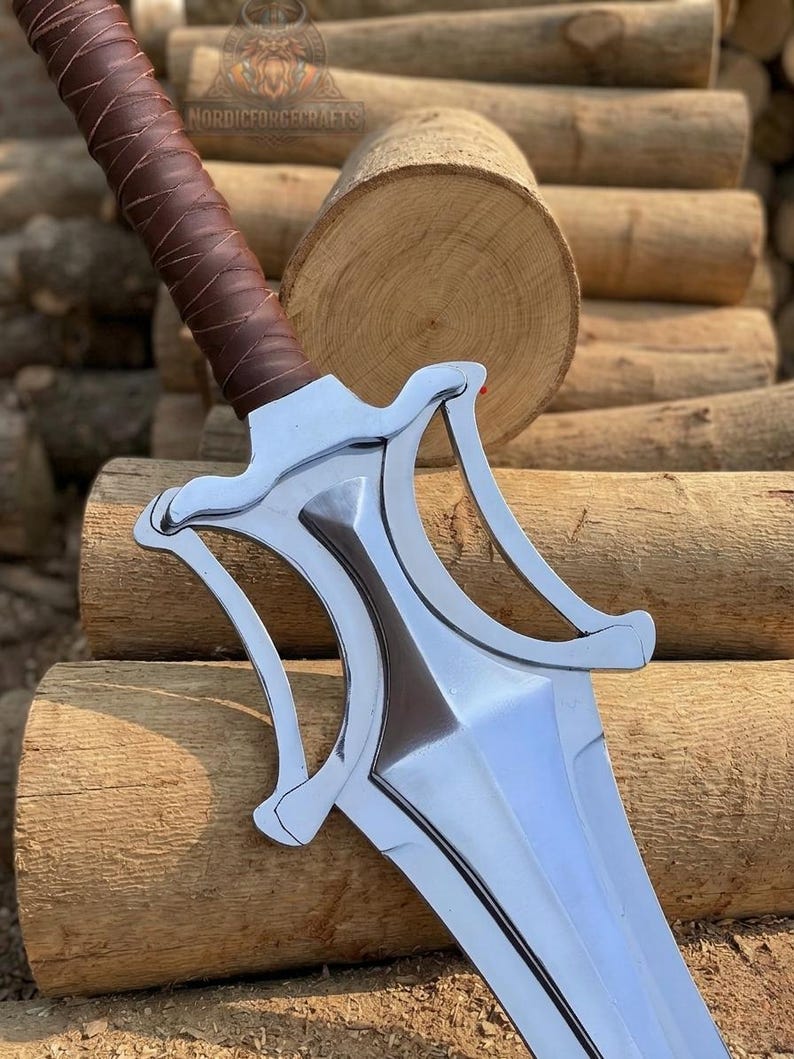 May include: A polished silver sword with a brown leather-wrapped handle. The blade has a distinctive shape with a central ridge and curved guard. The sword rests on a background of stacked wooden logs. The text "NORDICFORGECRAFTS" is visible.