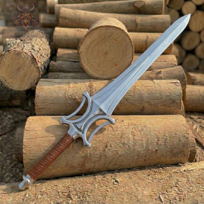 May include: A silver-colored sword with a brown leather-wrapped handle. The blade is long and pointed, with a decorative hilt. The sword is displayed on a bed of wooden logs. The text "NORDICFORGEFACTS" is visible in the upper left corner.