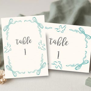 May include: A white ceramic mug with a black handle and the text "But First, Coffee" in a handwritten style. The mug is on a white surface. The mug is approximately 4 inches tall.