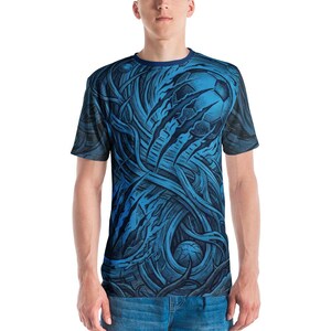 Könnte beinhalten: Ein blaues T-Shirt mit einem detaillierten, abstrakten Design. Die Grafik zeigt einen Fußball und Krallen, mit wirbelnden Linien und einem dunkelblauen Rundhalsausschnitt. Das T-Shirt wird von einer Person in blauen Jeans getragen.