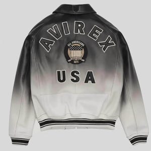 May include: A black and white ombre leather jacket featuring the text AVIREX in an arch across the upper back. Below the text is a circular patch with the words ALL AMERICANS and USA, followed by the letters USA in large black block lettering.