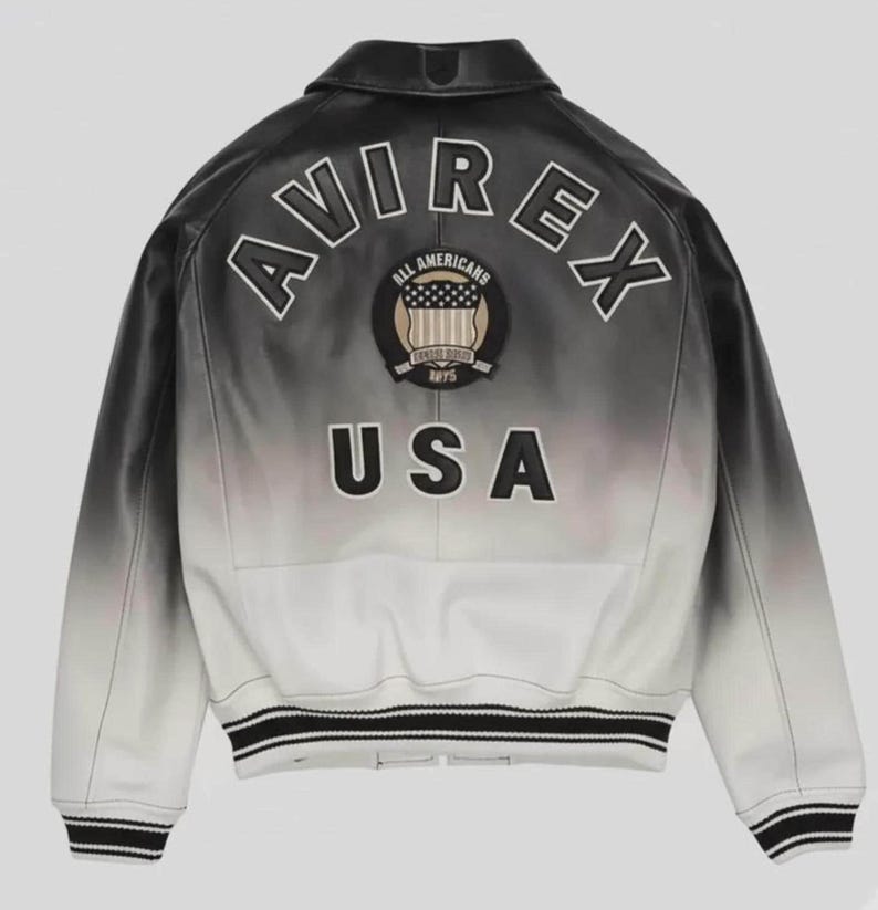May include: A black and white ombre leather jacket featuring the text AVIREX in an arch across the upper back. Below the text is a circular patch with the words ALL AMERICANS and USA, followed by the letters USA in large black block lettering.