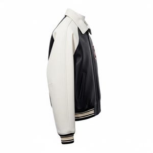 May include: A varsity jacket featuring a black body and contrasting white sleeves. The jacket has a classic collar, side pockets, and ribbed cuffs and hem with black and white stripes. A small circular patch is visible on the chest area.