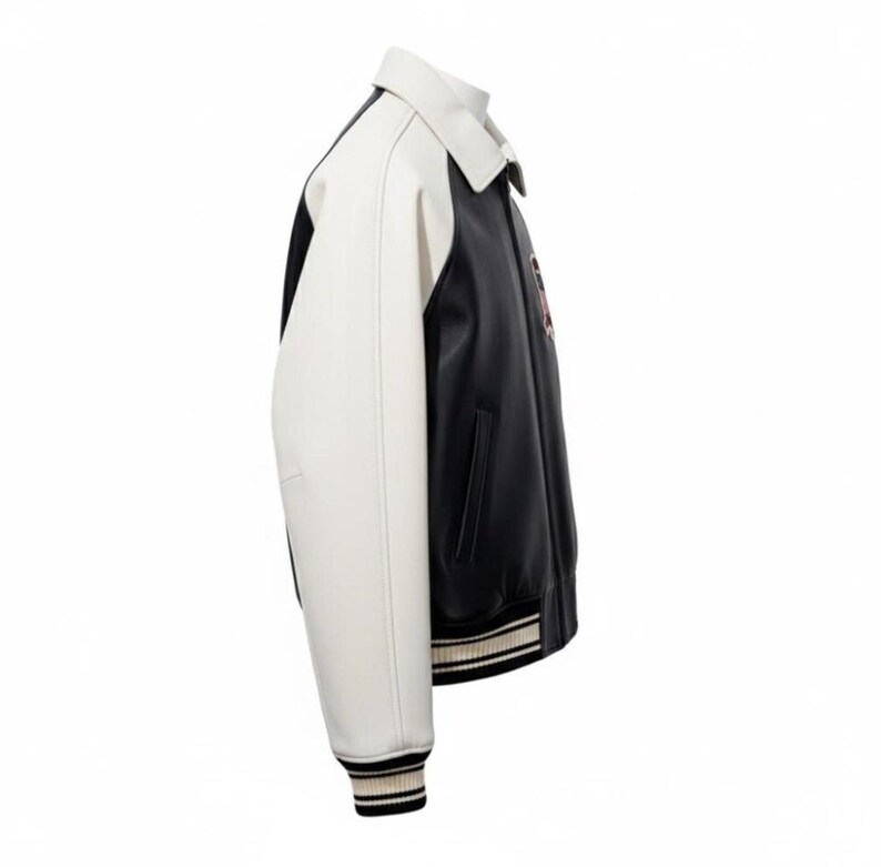 May include: A varsity jacket featuring a black body and contrasting white sleeves. The jacket has a classic collar, side pockets, and ribbed cuffs and hem with black and white stripes. A small circular patch is visible on the chest area.