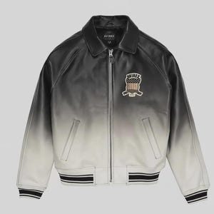 May include: A black and white ombre leather jacket featuring a full-length front zipper, a classic collar, and ribbed cuffs and hem with black and white stripes. An embroidered patch on the left chest displays the text AVIREX above a shield graphic.