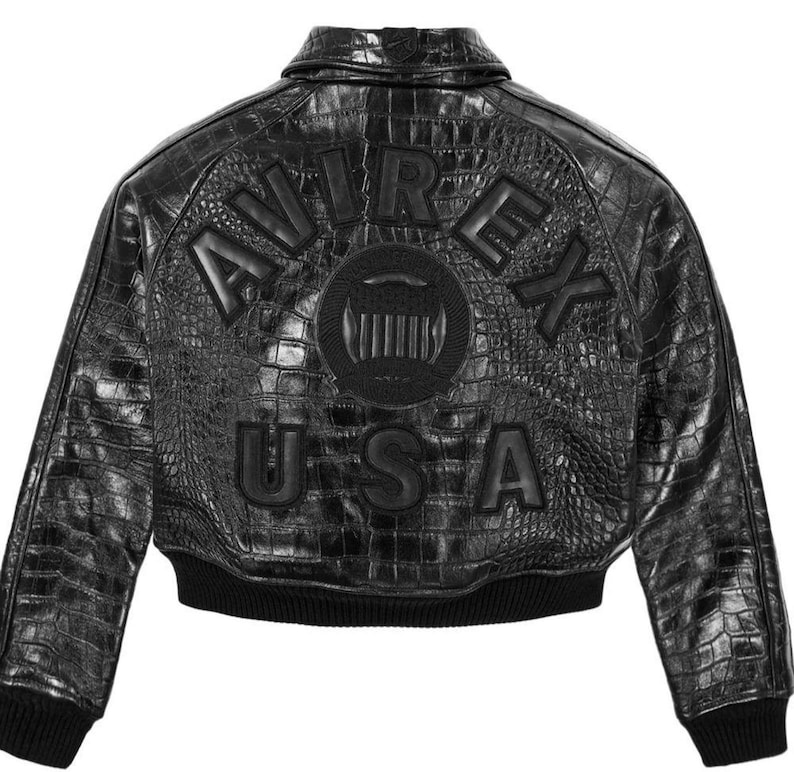 May include: A black leather jacket with a textured crocodile skin pattern. The back features the embossed text AVIREX USA in large letters and a circular emblem in the center. The jacket has a classic collar and black ribbed cuffs and hem.