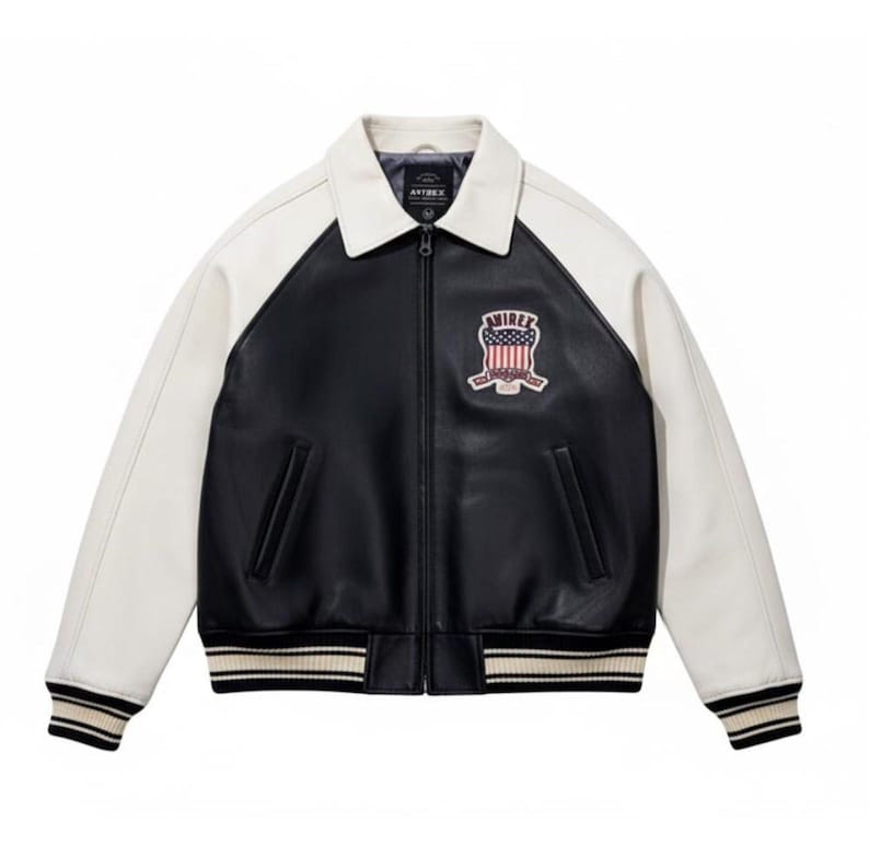 May include: A black and white jacket with a front zipper closure, a fold-down collar, and long sleeves. The chest features a patch with the text "AVIREX" above an American flag graphic. The cuffs and hem have black and white striped ribbing.