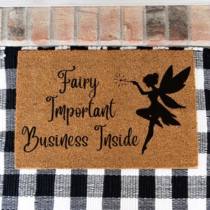 May include: A rectangular tan coir doormat featuring black text that reads Fairy Important Business Inside, accompanied by a black silhouette of a fairy holding a wand with a starburst tip, positioned on the right side of the mat.