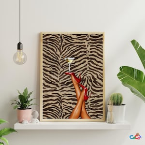 Könnte beinhalten: Gerahmter Druck mit einem Martini-Glas, das auf roten High Heels balanciert, mit Beinen in der Luft. Der Hintergrund hat ein Zebra-Streifenmuster in Braun und Beige. Der Druck befindet sich auf einem weißen Regal mit Pflanzen.
