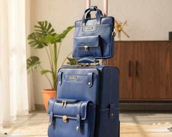 Op de afbeelding: Een bijpassende blauwe bagageset, bestaande uit een rolkoffer en een kleinere aktetas. De koffer heeft twee voorzakken en een uitschuifbare handgreep. De aktetas heeft een handvat aan de bovenkant en een schouderriem. Beide items hebben goudkleurige hardware.