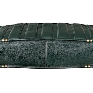 Puede incluir: Un bolso de cuero verde oscuro con una superficie texturizada y forma rectangular. La parte superior del bolso presenta l&iacute;neas verticales y paralelas cosidas. Se ven detalles met&aacute;licos dorados en los laterales.