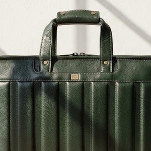 Puede incluir: Un malet&iacute;n de cuero verde oscuro con asa superior y bandolera desmontable. El malet&iacute;n tiene detalles de costuras verticales y herrajes dorados. El asa est&aacute; asegurada con remaches de lat&oacute;n. La bolsa est&aacute; dise&ntilde;ada para documentos y art&iacute;culos de negocios.