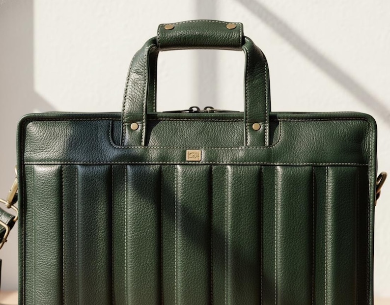 Puede incluir: Un malet&iacute;n de cuero verde oscuro con asa superior y bandolera desmontable. El malet&iacute;n tiene detalles de costuras verticales y herrajes dorados. El asa est&aacute; asegurada con remaches de lat&oacute;n. La bolsa est&aacute; dise&ntilde;ada para documentos y art&iacute;culos de negocios.
