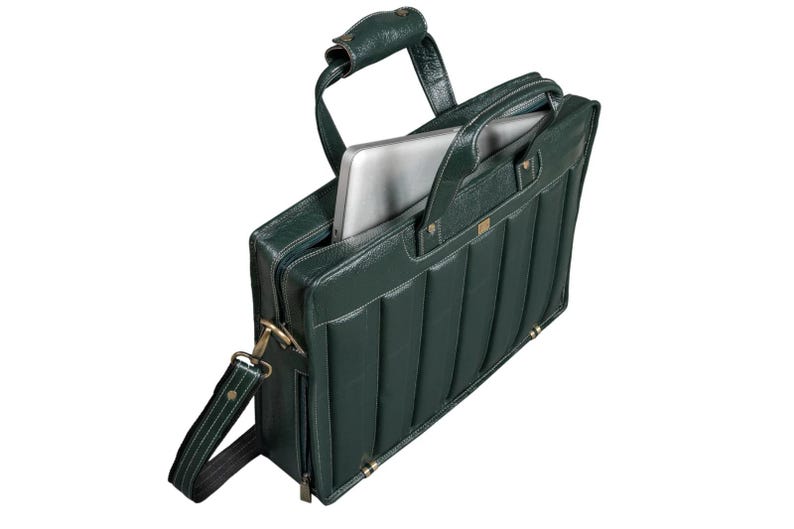 Puede incluir: Malet&iacute;n de cuero verde oscuro con un dise&ntilde;o acolchado. La bolsa tiene un asa superior, una correa para el hombro y un cierre de cremallera. Un port&aacute;til plateado es visible dentro del compartimento principal abierto. Los herrajes son dorados.