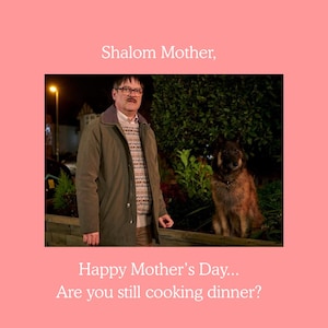 May include: A man wearing glasses, a sweater, and a green coat stands next to a dog. The image has text that reads "Shalom Mother, Happy Mother's Day... Are you still cooking dinner?" The background is a pink square.