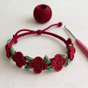 Può includere: Un braccialetto all'uncinetto fatto a mano con fiori bordeaux e foglie verdi. Il braccialetto regolabile è presentato con una palla di filo bordeaux e un uncinetto. Il design floreale è un accessorio affascinante.