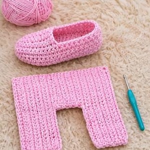 May include: A pink crochet slipper, a pink yarn ball, and a pink crochet rectangle are displayed on a textured surface. A teal crochet hook is also present. The slipper is in the shape of a shoe. The rectangle has a U-shaped cutout.