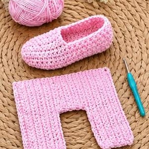 May include: A pink crocheted slipper, a matching rectangular piece, and a ball of pink yarn are arranged on a woven mat. A blue and silver crochet hook is also present. The slipper has a soft, fuzzy interior.