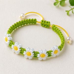 Peut inclure: Bracelet de marguerites fait à la main, avec des fleurs blanches et jaunes sur une bande verte tressée. Le bracelet a un cordon réglable jaune et blanc avec une perle à chaque extrémité. Un accessoire charmant.