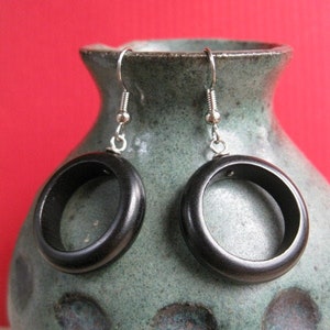 May include: A pair of black wooden earrings with silver hooks. The earrings are round and have a smooth finish.