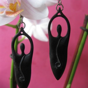 May include: A pair of black earrings shaped like a person in a yoga pose. The earrings are made of metal and have a smooth, polished finish.