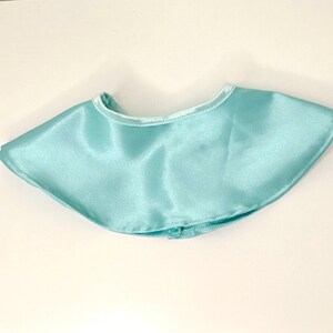 May include: A light blue satin cape with a rounded neckline. The cape is a solid color and has a smooth, shiny texture. The cape is designed to be worn around the neck and shoulders.