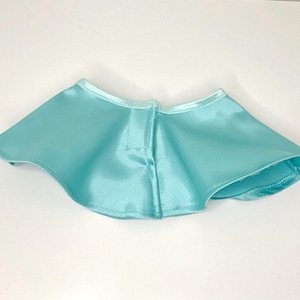 May include: A light blue satin cape with a rounded shape. The cape has a small collar and a button closure at the front. The fabric has a slight sheen, and the edges are neatly finished with a matching trim.