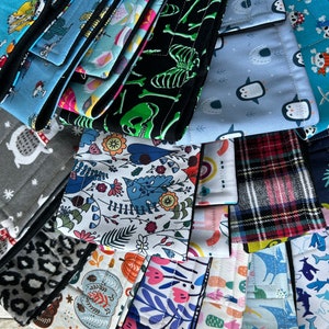 May include: A collection of colorful fabric scraps with various patterns, including penguins, skulls, flowers, and plaid. The fabrics are folded and stacked on top of each other.