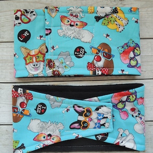 Puede incluir: Dos cintas para la cabeza de tela con temática de perros. La cinta superior está abierta y la inferior está cerrada. Ambas tienen un fondo azul claro con varias ilustraciones de perros con gafas de sol y pajaritas. El texto "I LOVE DOGS" es visible.