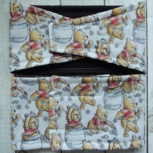 Puede incluir: Un artículo de tela con el tema de Winnie the Pooh, con un patrón repetido del oso con una camisa roja, botes de miel y detalles florales sobre un fondo blanco. El artículo tiene detalles en negro.