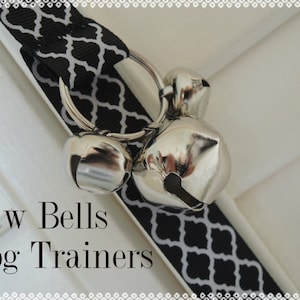 May include: A close-up of a dog training tool featuring a black and white patterned ribbon with silver bells. The text "Paw Bells Dog Trainers" is displayed in a serif font.