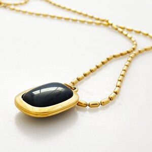 May include: A gold chain necklace with a dark blue gemstone pendant. The pendant is rectangular with a gold frame.