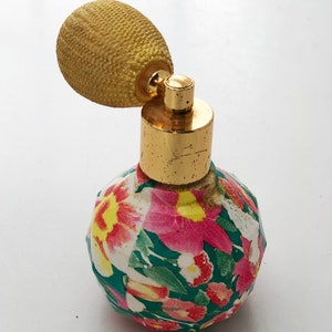 May include: A vintage floral perfume bottle with a gold top and a yellow atomizer. The bottle is round and has a green, pink, and white floral pattern.