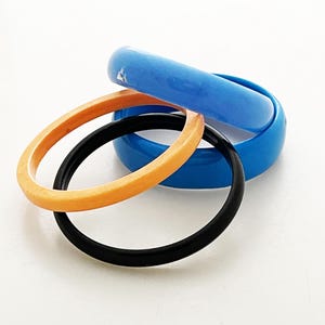 Könnte beinhalten: Vier Plastik-Armreifen in Blau, Orange und Schwarz. Die Armreifen sind übereinander gestapelt.