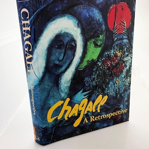 May include: A hardcover book titled "Chagall: A Retrospective" featuring a vibrant, surrealist painting in shades of blue, green, and red. The artist's name, "Chagall," is in yellow script.