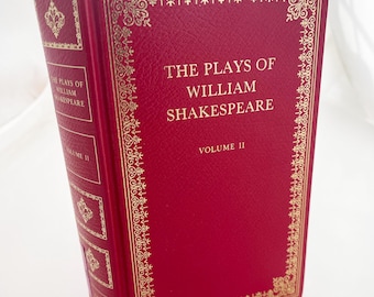 Puede incluir: Un libro de tapa dura rojo titulado "The Plays of William Shakespeare, Volumen II". El libro tiene detalles y texto decorativos dorados. El lomo también presenta el título y el número de volumen.