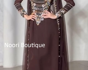 May include: A dark brown floor-length gown featuring long sleeves and a sheer overlay. The bodice and cuffs are heavily embellished with silver, gold, and dark beads and sequins. The text Noori Boutique is visible on the left side of the image.
