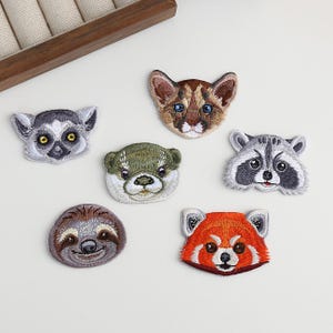 Pode incluir: Patches bordados com rostos de animais, incluindo um lêmure, puma, lontra, guaxinim, bicho-preguiça e panda-vermelho. Cada patch apresenta costuras detalhadas e cores vibrantes, perfeitos para adicionar a roupas ou acessórios.