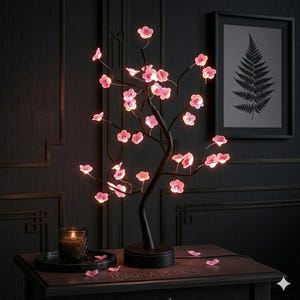 May include: A black cherry blossom LED tree lamp with pink illuminated flowers. The lamp is on a dark wooden nightstand with a candle and a framed fern print in the background. The text "Lumina Petals" is visible.