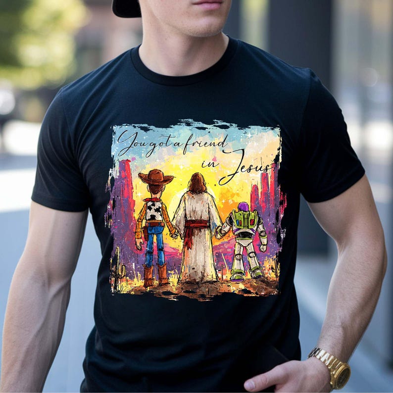 May include: Black t-shirt featuring a colorful graphic of three figures: a cowboy, Jesus, and a space ranger, holding hands. The text "You got a friend in Jesus" is above the figures. The design has a painted look.