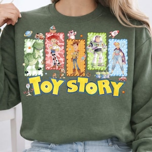 May include: Green sweatshirt featuring the words "Toy Story" in yellow block letters. The sweatshirt has a colorful graphic of characters from the animated film, including Rex, Jessie, Woody, Buzz Lightyear, and Bo Peep.