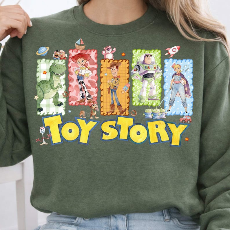 May include: Green sweatshirt featuring the words "Toy Story" in yellow block letters. The sweatshirt has a colorful graphic of characters from the animated film, including Rex, Jessie, Woody, Buzz Lightyear, and Bo Peep.