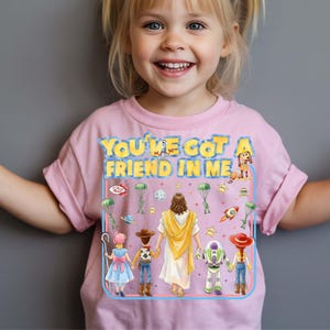 May include: Pink t-shirt with the text "YOU'VE GOT A FRIEND IN ME" and cartoon illustrations of characters. The design includes a dog, a rocket, and other playful elements. The shirt is worn by a young child.