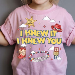 以下が含まれることがあります： I KNEW IT I KNEW YOUの文字、INFINITY AND BEYONDと書かれた黄色い保安官バッジ、赤いカウボーイハット、赤いカウボーイブーツ、YOU'VE GOT A FRIEND IN MEと書かれたビーズブレスレット、積み木がプリントされたライトピンクのTシャツ。