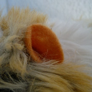 May include: Close-up of a plush toy with white and brown fur. The toy has an orange felt ear.