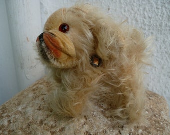 Puede incluir: Un perro de peluche vintage con pelaje blanco y nariz marrón. El perro tiene un ojo de vidrio rojo y una pequeña etiqueta en la espalda.