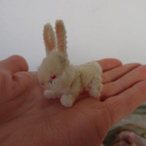 Puede incluir: Un pequeño conejito de peluche blanco con ojos rojos. El conejito está hecho de limpiapipas y está sentado en una mano.