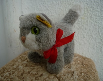 Steiff, piccolo gattino di peluche grigio/bianco con grandi occhi verdi, bottone argentato, vecchia etichetta gialla e fiocco rosso originale.