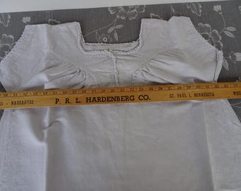 May include: A white cotton nightgown with a lace trim around the neckline and sleeves. The nightgown has a button closure at the neckline. The nightgown is lying flat on a patterned surface.